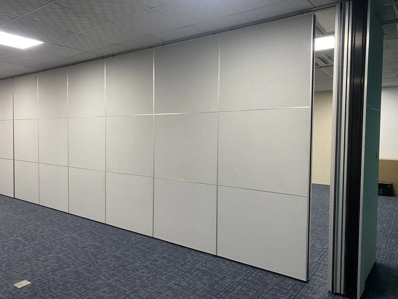 The end panel of an operable wall swung open in a Manila office, showing the aluminium edge profile and the overhead track at the ceiling line