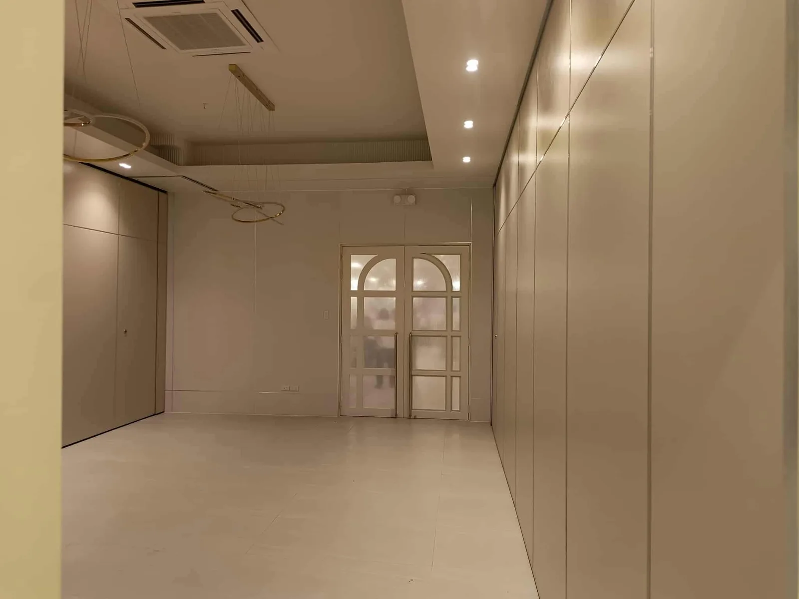 A closed run of operable wall panels lining a Metro Manila venue interior, with arched fluted-glass doors beyond
